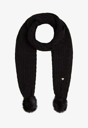 Écharpe noire tricotée avec motif torsadé, deux pompons duveteux aux extrémités, et un petit charm métallique en forme de cœur sur un côté.