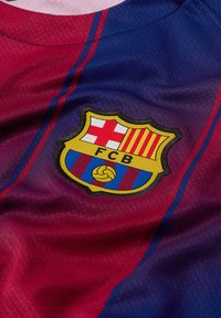 FC Barcelonas tröja med vinröda och blå färger med horisontella ränder. Inkluderar en framträdande logotyp med röda och gula accenter. Texturerad tyg.
