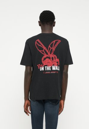 Schwarzes Baumwoll-T-Shirt mit einem roten Grafikmotiv einer Fliege mit großen Flügeln auf dem Rücken, darunter in Weiß der Schriftzug "Fly On The Wall".