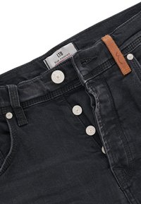 Svarta denimjeans med knappstängning, prydda med ett märkeslabel, ljusa sömmar och en brun läderdetalj vid midjan.