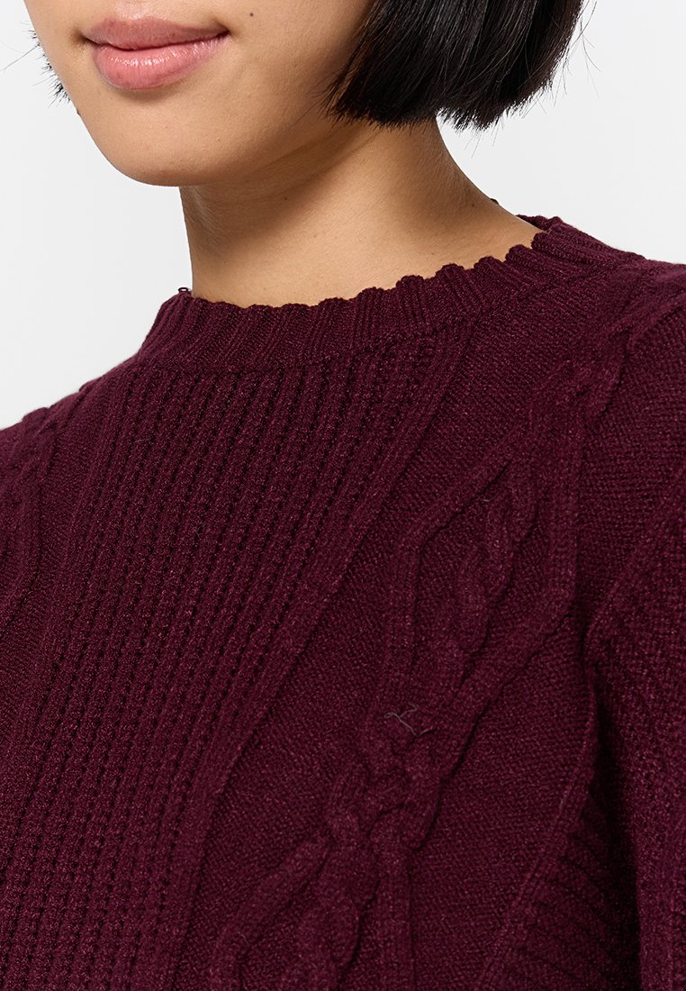 Maglione lavorato a maglia color bordeaux con design a coste e a trecce, dotato di scollatura ondulata. Tessuto morbido, caldo e con dettagli curati.