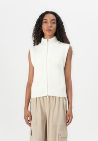 Débardeur en tricot sans manches crème avec un col haut et une fermeture éclair à l'avant, présentant un motif texturé et un ourlet côtelé. Idéal pour les tenues en couches.