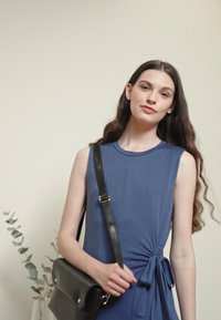 Vestido azul sem mangas com um detalhe de nó lateral, combinado com uma bolsa preta de ombro. Tecido suave, corte descontraído e design minimalista.