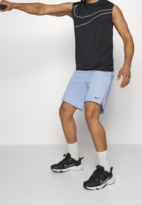 Haut de sport noir sans manches avec accents blancs, associé à un short bleu clair. Chaussures noires et chaussettes blanches complètent la tenue.