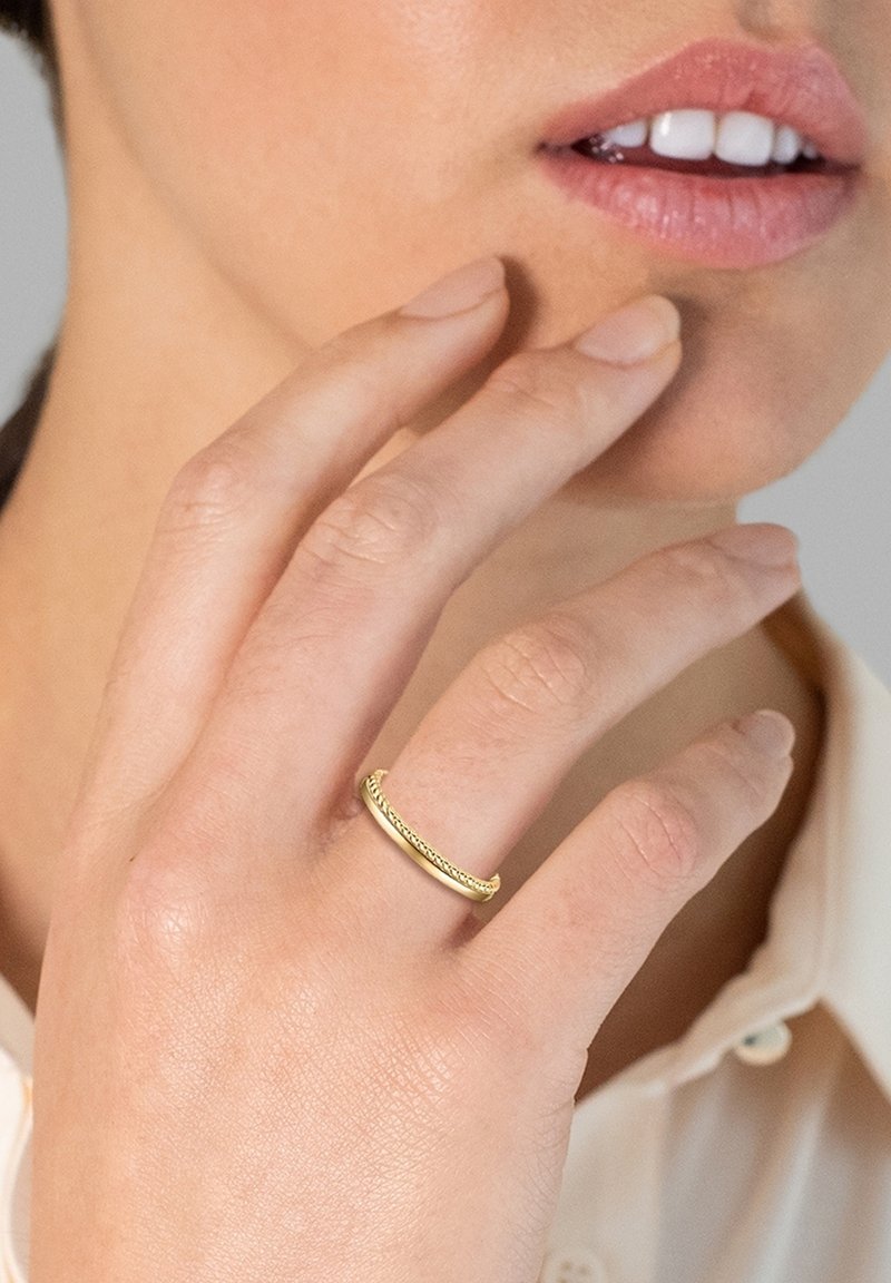 Gold ring with a twisted texture, worn on a finger. Close-up view with soft skin tones and a neutral backdrop, highlighting the ring's design.