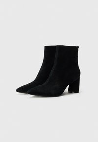 Sorte ankelstøvler i suede med spisse tå, en midt-høy blokkhel og minimale sømdetaljer. Glatt tekstur med en matt finish.