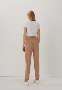 Braune gestrickte Hose mit lockerer Passform, hohem Bund und seitlichen Taschen, kombiniert mit einem weißen T-Shirt und weißen Sneakers.