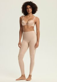 Nude, bezszwowy biustonosz z cienkimi ramiączkami w komplecie z pasującymi legginsami z wysokim stanem; gładka tekstura, dopasowany krój.