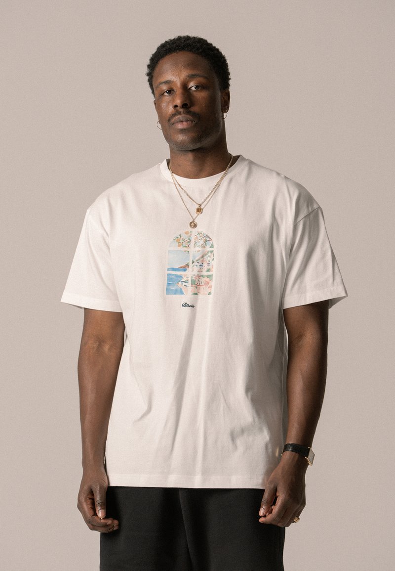 T-shirt kratkih rukava od bijelog pamuka s šarenom grafikom prozora koja na sredini sadrži cvjetne i pejzažne elemente.