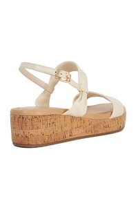 Beige plateau sandalen met een kurken hak, voorzien van een gekruisd bandjesontwerp en een gouden gesp op een verstelbare enkelband. Glad textuur.