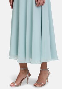 Jasnoniebieska, zwiewna sukienka z szyfonu z warstwowym dołem, w połączeniu z błyszczącymi srebrnymi sandałami na szpilce. Gładka faktura, smukła sylwetka.