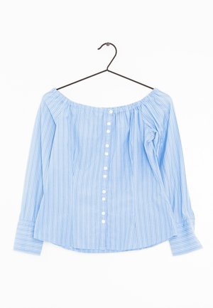Jasnoniebieska bluzka z odkrytymi ramionami z białymi pionowymi paskami i rzędem białych guzików z przodu, wisząca na czarnym wieszaku.