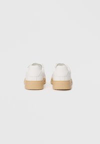 Hvite joggesko med en glatt lær-overdel og en beige gummisåle, med avrundede bakker og subtil merkevare på hælen.