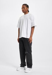 Camiseta blanca de gran tamaño, vaqueros negros desgastados y zapatillas blancas con acentos grises; diseño minimalista y corte relajado.