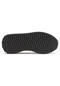 Semelle de chaussure en caoutchouc noir avec motif de bande de roulement en zigzag et texte "new balance" répété sur toute la semelle, vue de dessous.