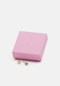 Goldfarbene Ohrringe mit Kristallakzenten neben einer strukturierten pinken Geschenkbox mit einem eingeprägten Logo auf dem Deckel. Die Box hat eine quadratische Form.