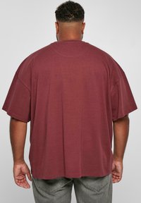 Burgundské oversized tričko s krátkými rukávy a kulatým výstřihem, vyrobené z měkké tkaniny. Má uvolněný střih a hladkou strukturu.