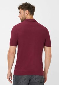 Polo rosso borgogna con maniche corte, materiale testurizzato e colletto classico. Presenta un piccolo logo sul lato sinistro in basso.