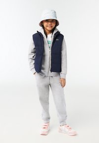 Gilet imbottito navy su felpa grigia con pantaloni della tuta, abbinato a sneakers rosa. Il cappello a secchiello è azzurro chiaro con dettagli decorativi sottili.