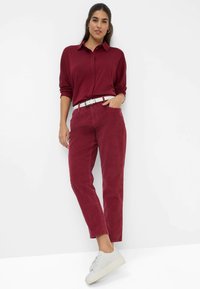 Pantaloni in corduroy bordeaux con una vestibilità comoda, abbinati a una camicia button-up color amaranto e una cintura bianca. Sneakers grigie completano l'outfit.