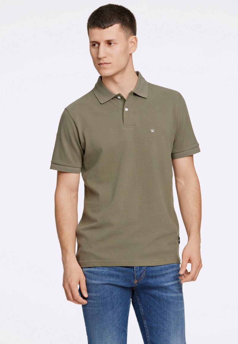 Olijfgroene polo met kraag, korte mouwen en een klein logo op de borst. Gecombineerd met blauwe jeans. Zachte textuur.