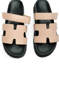Vegan leather slide sandals in pale pink, featuring cut-out designs and a black rubber sole. Adjustable strap for a secure fit.