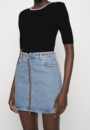 Mujer con top negro de manga corta acanalado con ribete blanco y minifalda de mezclilla azul claro de cintura alta con cremallera frontal.