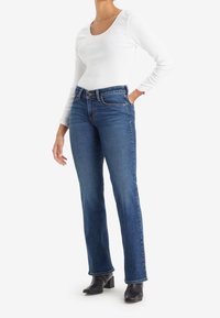 Jeans de mezclilla azul con un corte recto, que cuentan con una cintura de media altura, diseño de cinco bolsillos y detalles de costura mínimos, combinados con una blusa blanca de manga larga.
