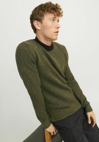 Knit sweater in dark green with a textured finish, contrasting black crew neckline, and fitted silhouette. Features long sleeves and ribbed hem.