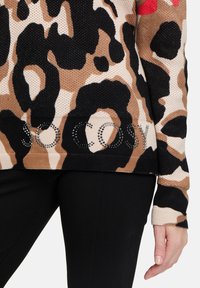 Knit sweater in a leopard print with black, beige, and brown tones. Features "SO COSY" in rhinestones at the hem. Textured fabric.