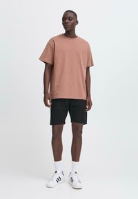 Lichtbruin oversized t-shirt, zwarte shorts, witte sokken en witte sneakers. Eenvoudig ontwerp, casual pasvorm en minimalistische stijl.