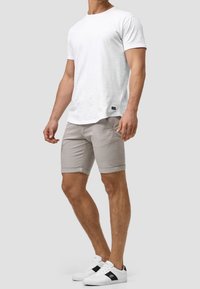 T-shirt en coton blanc à manches courtes, shorts gris ajustés avec des ourlets retournés, et baskets blanches avec des accents noirs. Design simple.