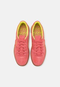 Chaussures de sport en daim rose avec des accents jaunes, dotées d'un laçage, d'une languette rembourrée et d'une semelle extérieure en caoutchouc gomme texturée.