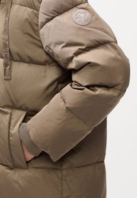 Brown puffer jacket with a quilted design, featuring a ribbed cuff and an embroidered logo patch on the upper arm. Smooth texture.