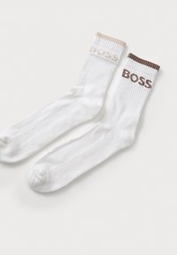 Fehér zoknik bordás textúrával, kontrasztos bézs és barna díszítéssel a tetején, valamint a "BOSS" logóval nyomtatva minden mandzsettán.