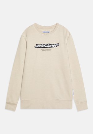 Sudadera beige con cuello redondo, mangas largas y puños acanalados, que presenta un destacado logotipo negro en la parte delantera. Textura suave, diseño casual.