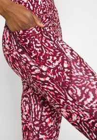 Legginsy w kolorze burgundowym i różowym, z abstrakcyjnym wzorem, wykonane z elastycznego materiału, z boczną kieszenią i płaskimi szwami dla komfortu.