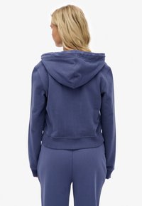 Granatowa krótka bluza z kapturem wykonana z miękkiego materiału, z szerokim kapturem, ściągaczem u dołu i długimi rękawami, widoczna od tyłu z minimalnymi ozdobami.