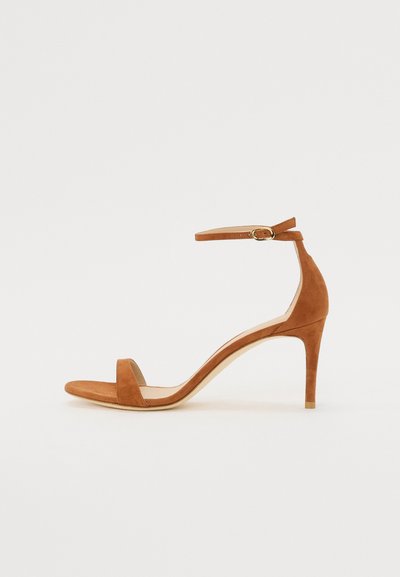 Sandale à talons hauts en daim marron avec une fine bride de cheville et une boucle dorée, bout ouvert et un design épuré et minimaliste.