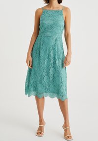 Lace dress in teal with thin spaghetti straps, fitted bodice, A-line shape, scalloped hem, features floral patterns throughout.