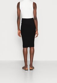 Jupe midi noire à côtes avec une silhouette ajustée, dotée d'une taille élastique, portée avec des sandales plates, vue de l'arrière.