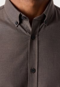 Gros plan d'une personne portant une chemise gris foncé boutonnée avec un col boutonné et des boutons noirs.