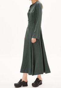 Vihreä pitkähihaiset mekko, jossa istuva yläosa ja laskeutuva helma; valmistettu pehmeästä kankaasta. Yhdistetty mustien paksukorkoisten klomppien kanssa.