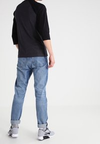 Svart och grå ¾-sleeve skjorta ihop med ljusblå denimjeans, rullade ärmslut, och grå sneakers med svarta detaljer. Enkelt avslappnat outfit.