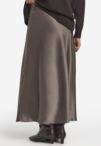 Szara maxi spódnica z satyny o gładkiej fakturze, zwiewnym kroju i rozcięciu z boku, zestawiona z czarnymi botkami za kostkę.