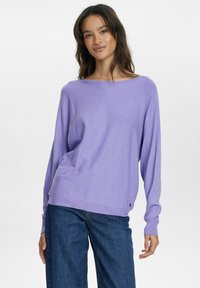 Lila, långärmad tröja med vid halsringning och avslappnad passform. Mjuk textur, parat med mörkblå vida jeans.
