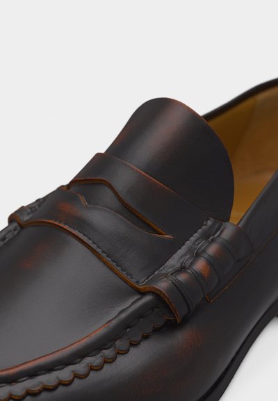 Κοντινό πλάνο ενός μοκασίνι από σκούρο καφέ δέρμα με λεπτομερή ραφή και σχισμή για πένι στο πάνω μέρος.