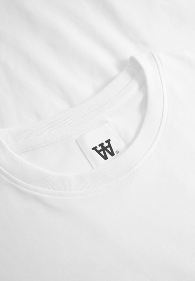 Weißes Baumwoll-T-Shirt mit geripptem Rundhalsausschnitt, das ein kleines, schwarzes rechteckiges Etikett an den inneren Kragen genäht hat. Glatte Textur.