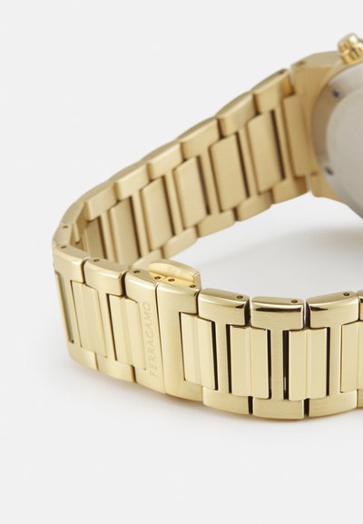 Orologio in metallo dorato con bracciale a maglie, caratterizzato da finiture lucidate e opache, e cassa in acciaio inossidabile. Include il marchio inciso.