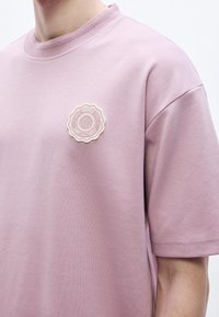 Svetloružové tričko s krátkym rukávom z bavlnenej zmesi, na hrudi s okrúhlym krémovo sfarbeným vyšívaným logom.